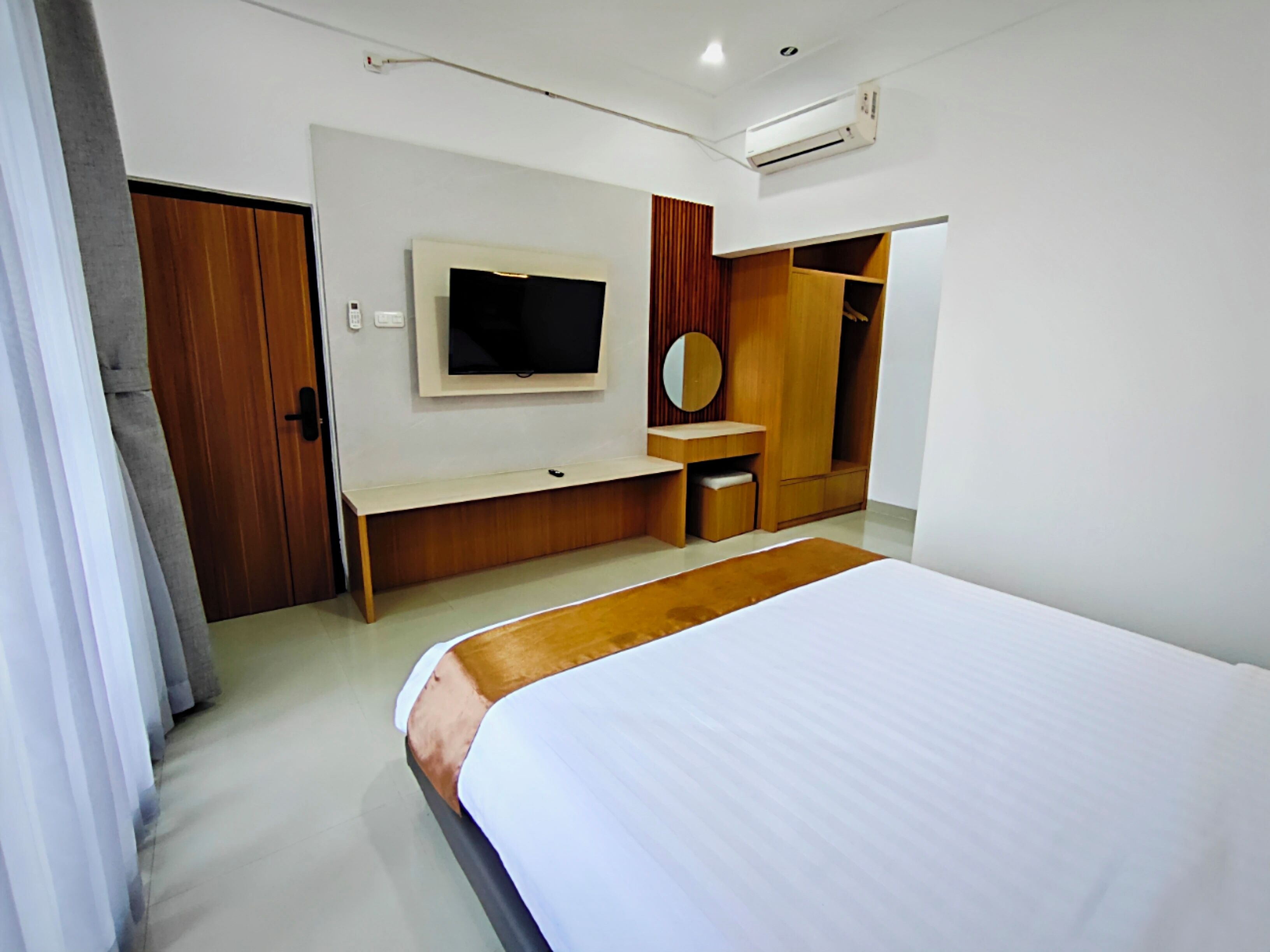 Ein modernes Schlafzimmer mit einem großen Bett, einem an der Wand montierten Fernseher, einem Holzschrank und einem kleinen Schreibtisch.