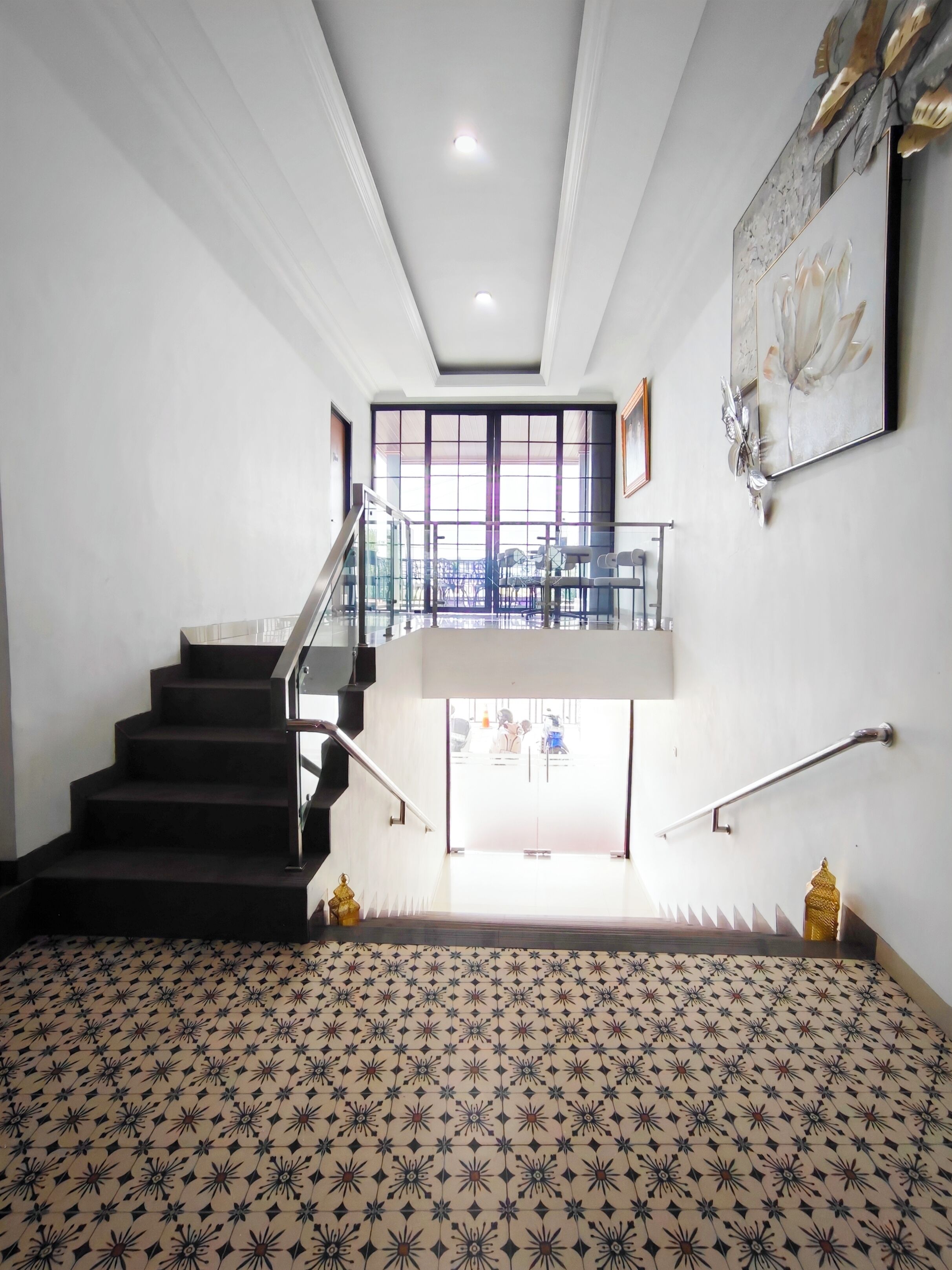A spacious interior with a patterned floor, a staircase leading to a balcony, and a view of the outside.