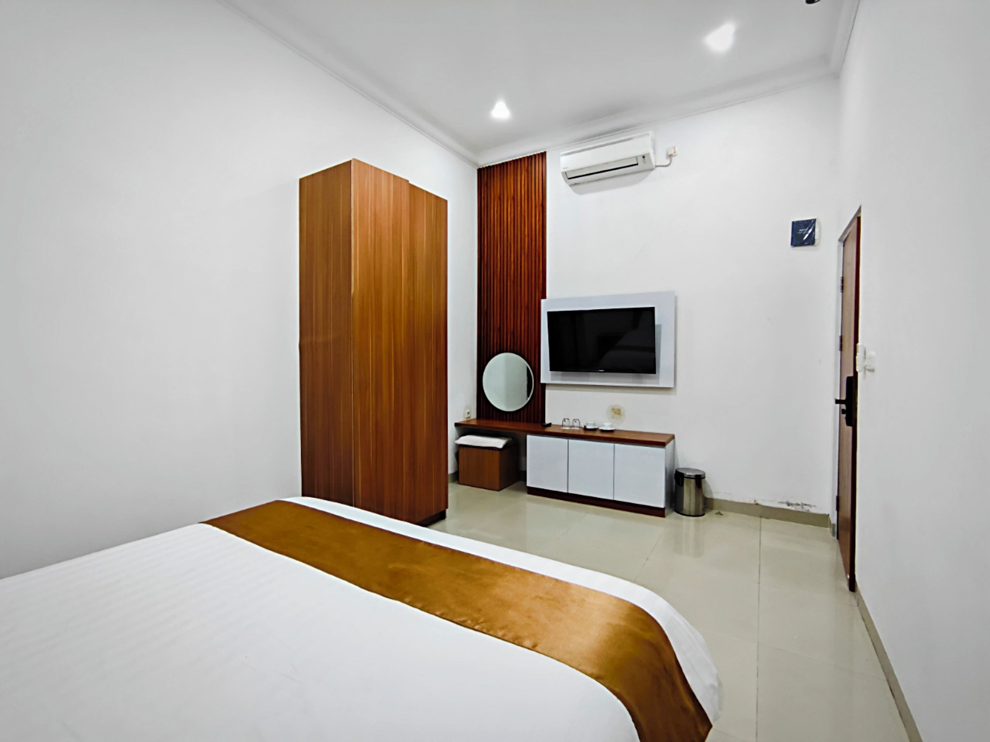 Una habitación de hotel moderna con una cama grande, un armario de madera, un televisor y un baño pequeño.