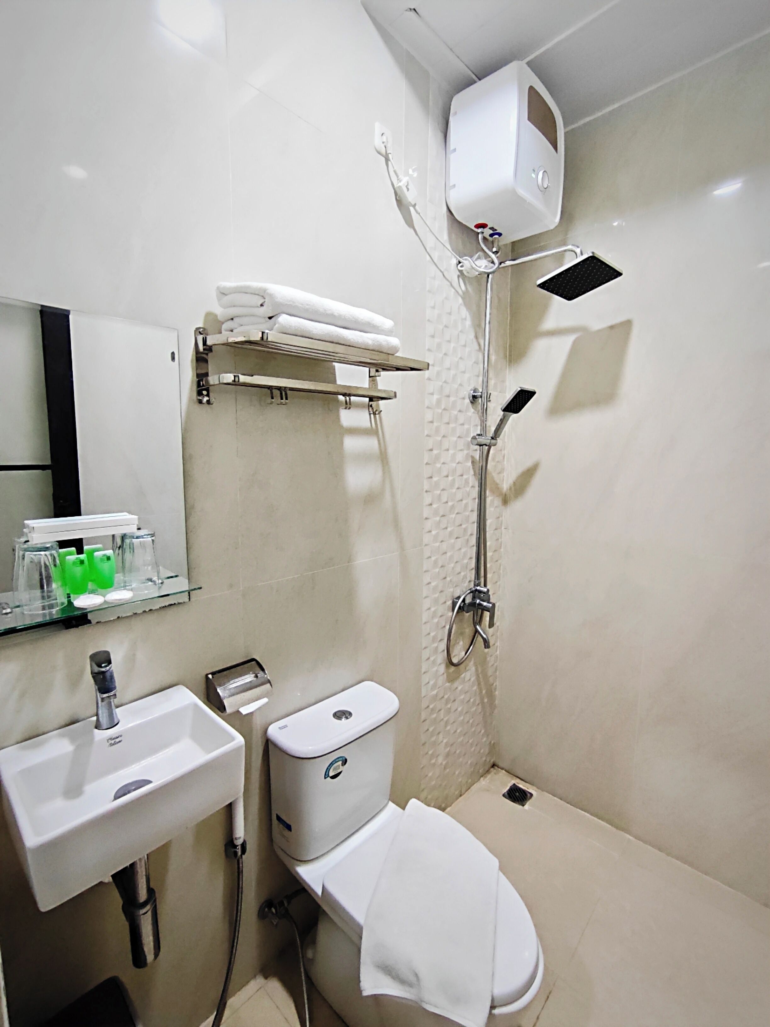 Une salle de bain équipée d’un lavabo, de toilettes et d’une douche. On y trouve un porte-serviettes au-dessus des toilettes et une étagère avec des articles de toilette.