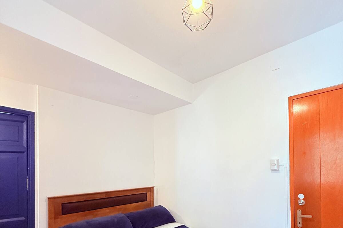 Ein ordentlich bezogenes Bett mit Holz-Kopfteil, einem gerollten Handtuch und einer hängenden Leuchte.