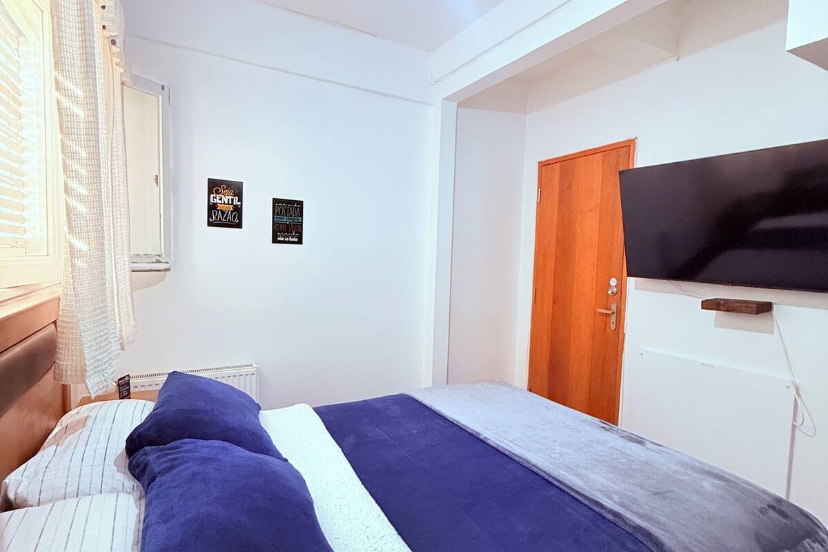 Ein Schlafzimmer mit einem Bett, einer Holztür, einem weißen Heizkörper und einem an der Wand befestigten Fernseher.