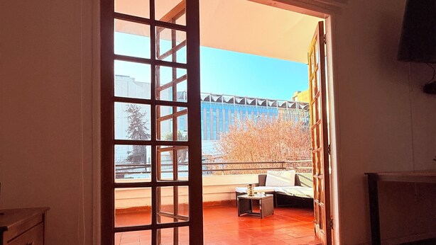 A room with a wooden herringbone floor, a sliding glass door leading to an outdoor area with a view of a building and trees. - Maktvb Europa Hostal Boutique (Santiago)