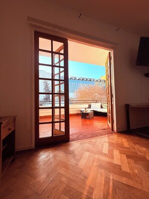 A room with a wooden herringbone floor, a sliding glass door leading to an outdoor area with a view of a building and trees. - Maktvb Europa Hostal Boutique (Santiago)