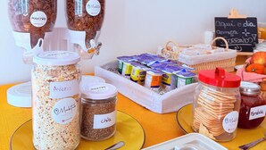 A table with various food items including jars of granola, chia seeds, and crackers, along with a coffee machine and a chalkboard menu. - Maktvb Europa Hostal Boutique (Santiago)