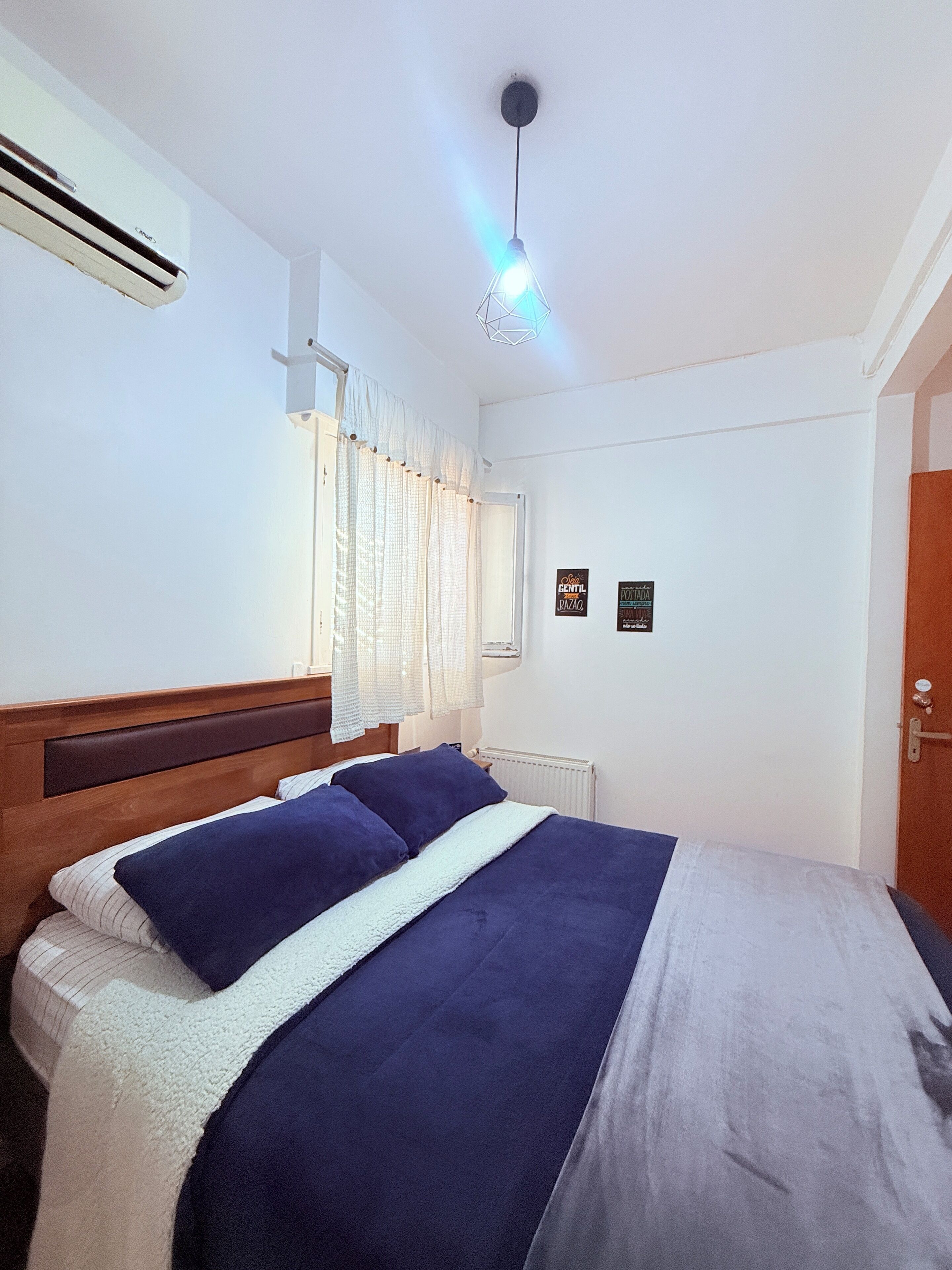 Une chambre à coucher avec un lit, une fenêtre avec des rideaux, un radiateur et un climatiseur fixé au mur.