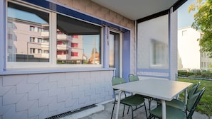 A modern outdoor dining area with a white table and green chairs, a sliding glass door, and a view of a residential building in the background. - Blueground | Dietikon, balcony, nr Bahnhof (Zurich)