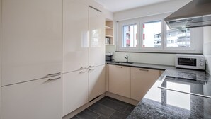 A modern kitchen with white cabinets, a granite countertop, a built-in microwave, and a window with a view of buildings. - Blueground | Dietikon, balcony, nr Bahnhof (Zurich)