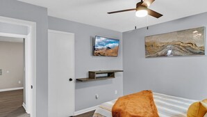 A bedroom with a bed, a mounted TV, a ceiling fan, and artwork on the wall.