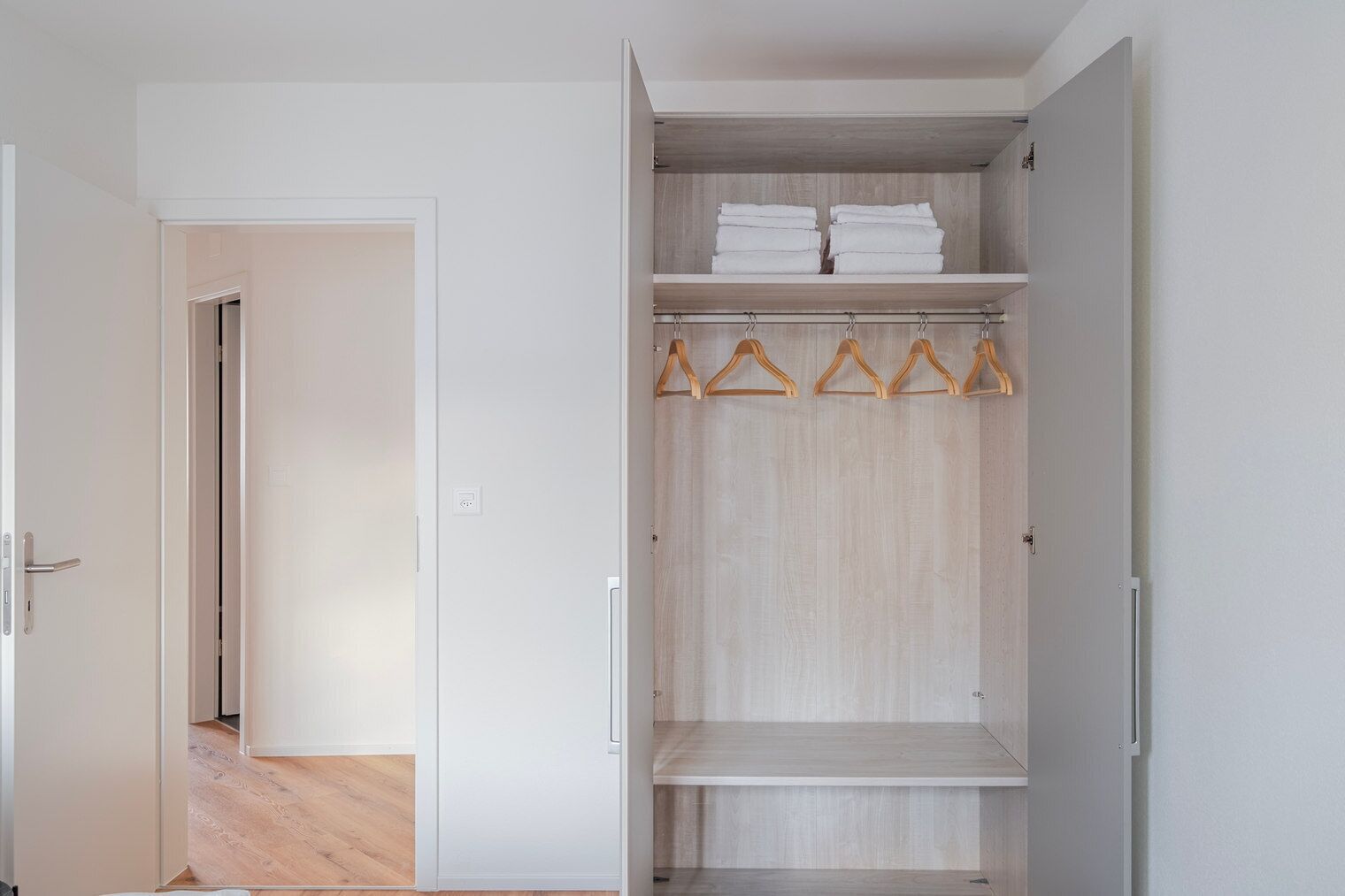 Een inloopkast met houten planken, een kledingroede en een deur naar een andere kamer.