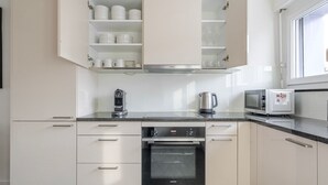 Uma cozinha moderna com armários brancos, forno embutido, máquina de café, chaleira e micro-ondas.