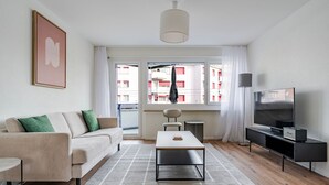 Uma sala de estar moderna com sofá, mesa de centro, TV e uma janela grande com vista para edifícios.