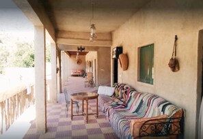 A covered outdoor seating area with a checkered floor, a sofa, and a table. - Gite jawaher aguerd (Aqesri)