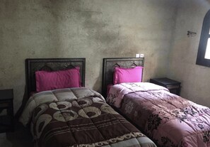 A small, dimly lit room with two single beds, each with a headboard and a bedside table. - Gite jawaher aguerd (Aqesri)