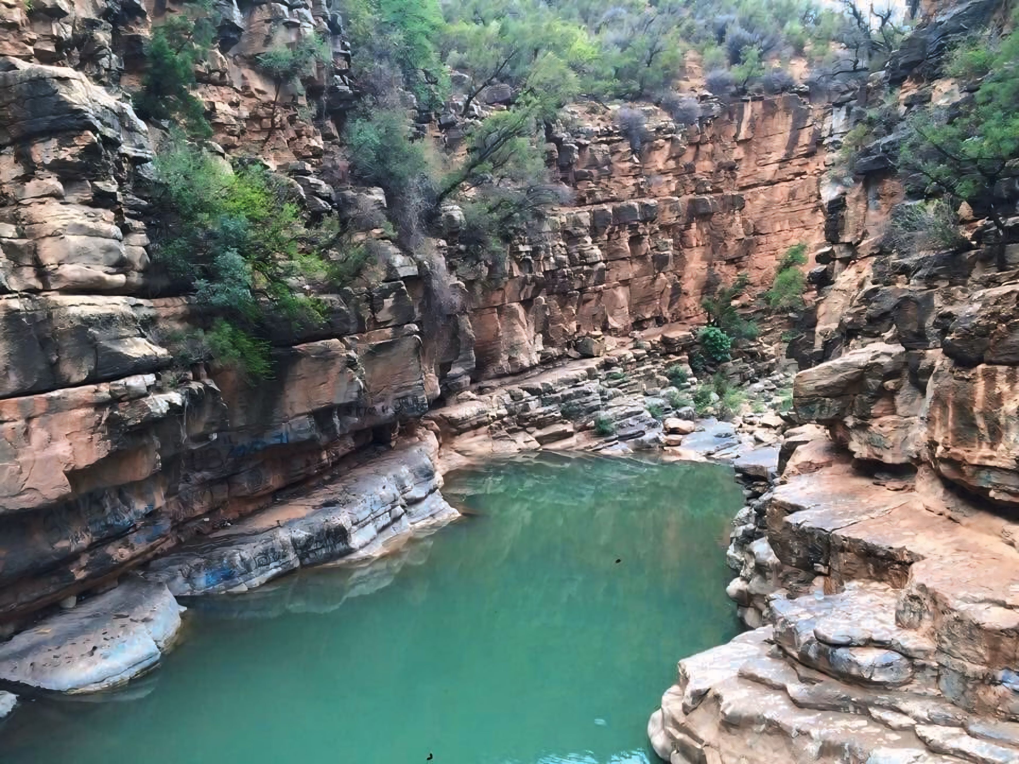 A canyon with a clear pool surrounded by rocky cliffs and sparse vegetation.