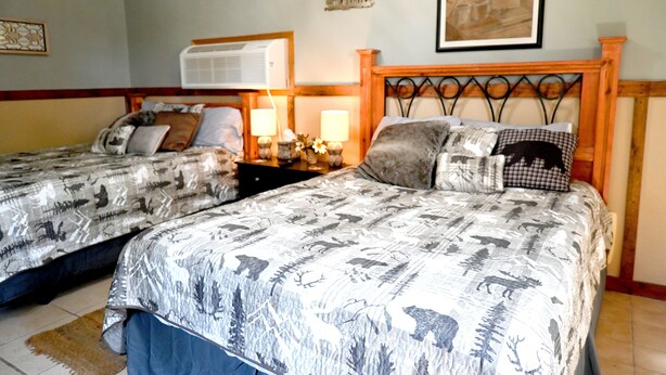Een hotelkamer met twee bedden, elk voorzien van beddengoed met een patroon en een houten hoofdbord. Er staat een nachtkastje met lampen en een tafeltje met een bloemenarrangement.