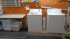 Een wasruimte met twee wasmachines, opbergbakken van plastic en planken met schoonmaakmiddelen.