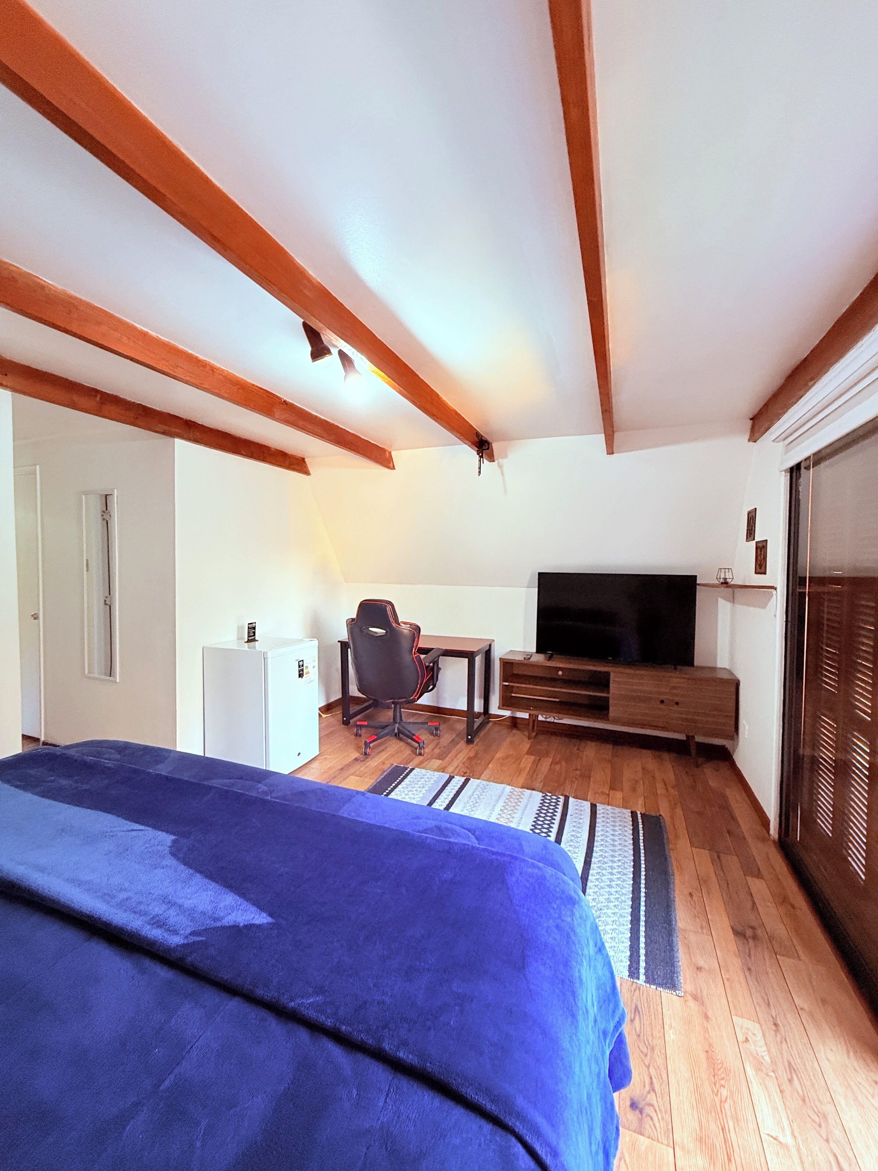 Een kamer met een bed, een bureau, een stoel, een televisie en een kledingkast.
