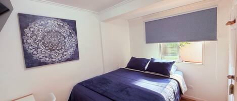 Un dormitorio con una cama, una lámpara en el techo, una ventana con persiana y una obra de arte colgada en la pared.