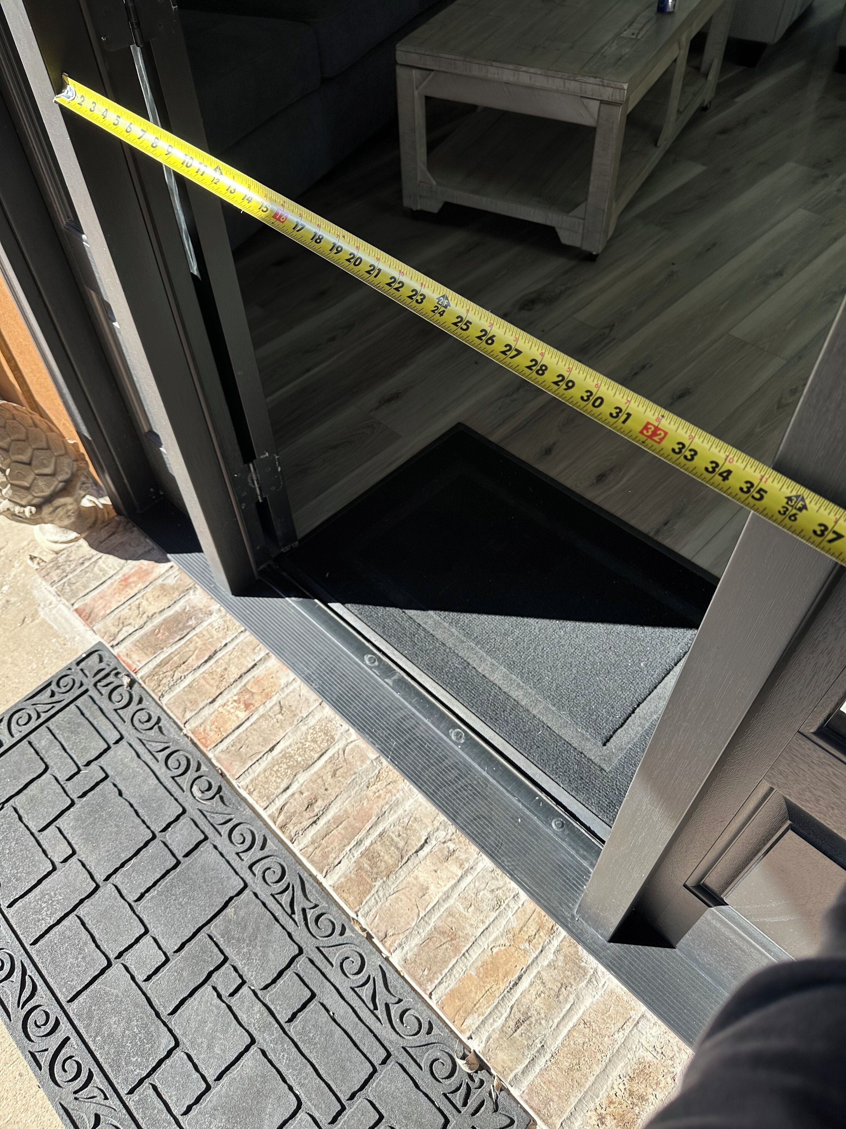Un mètre ruban tendu à travers l’encadrement d’une porte, une petite table et un tapis à motifs.