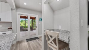 Une cuisine dotée de plans de travail en granit, un coin repas avec une chaise et une porte-fenêtre coulissante donnant sur une terrasse extérieure.