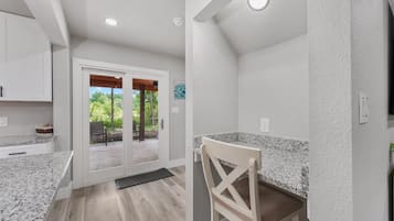 Une cuisine dotée de plans de travail en granit, un coin repas avec une chaise et une porte-fenêtre coulissante donnant sur une terrasse extérieure.