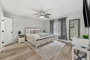 A bedroom with a bed, bedside table, nightstand, ceiling fan, and a mirror.
