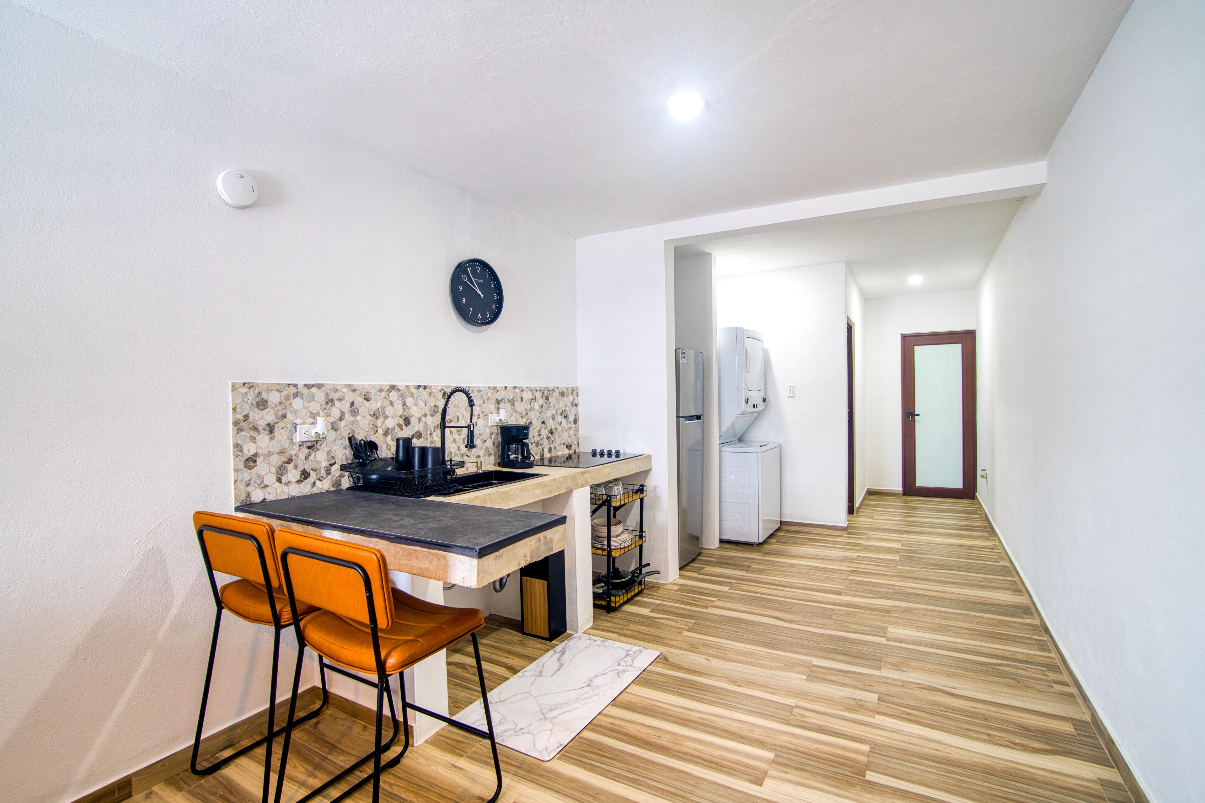 A compact kitchen with a dining area, a clock, and a refrigerator.