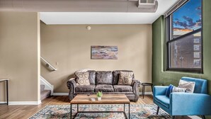 A living room with a brown leather couch, a blue armchair, a wooden coffee table, and a colorful rug.