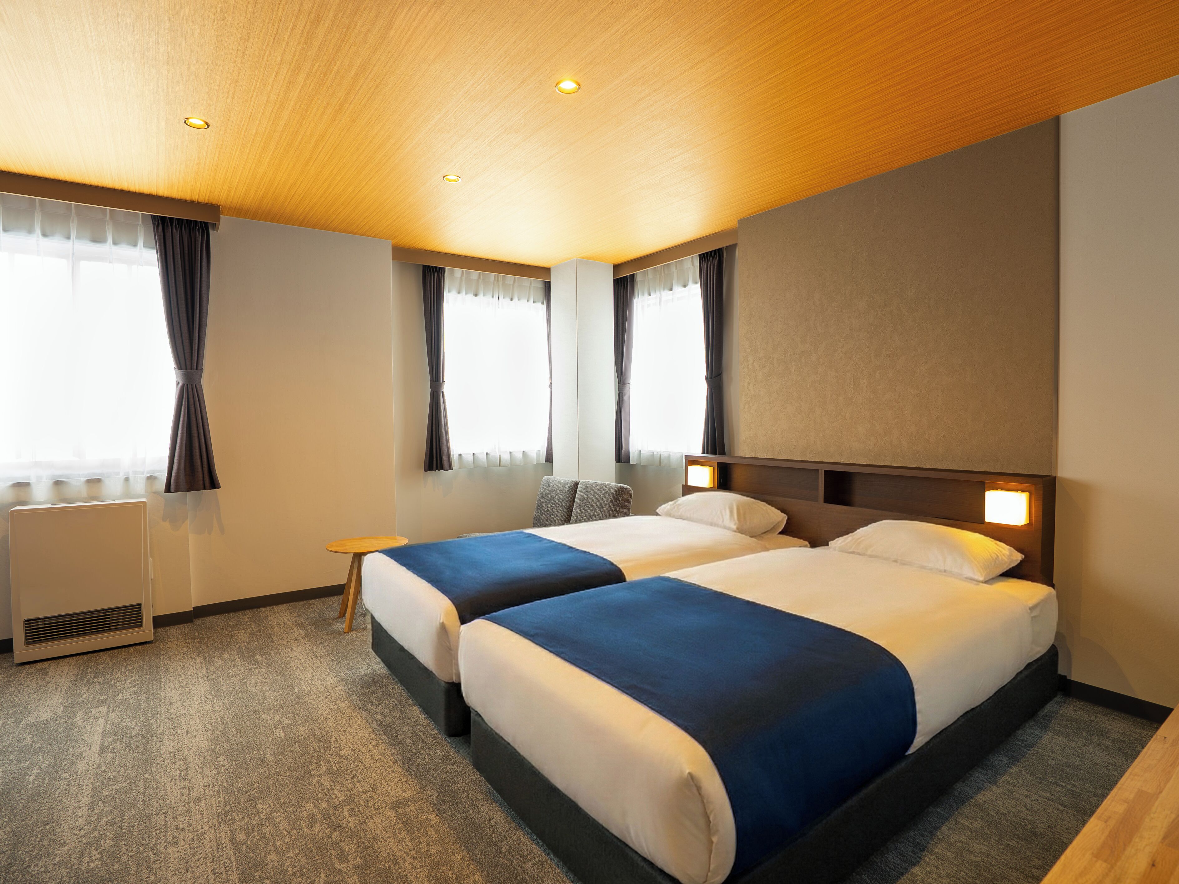 A hotel room with two beds, a small table, and a heater.