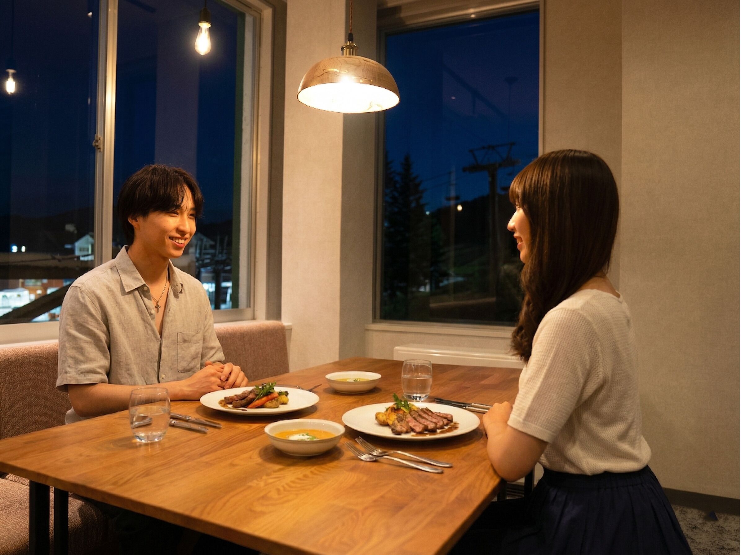 A dining table with plates of food, a glass of water, and a pendant light.