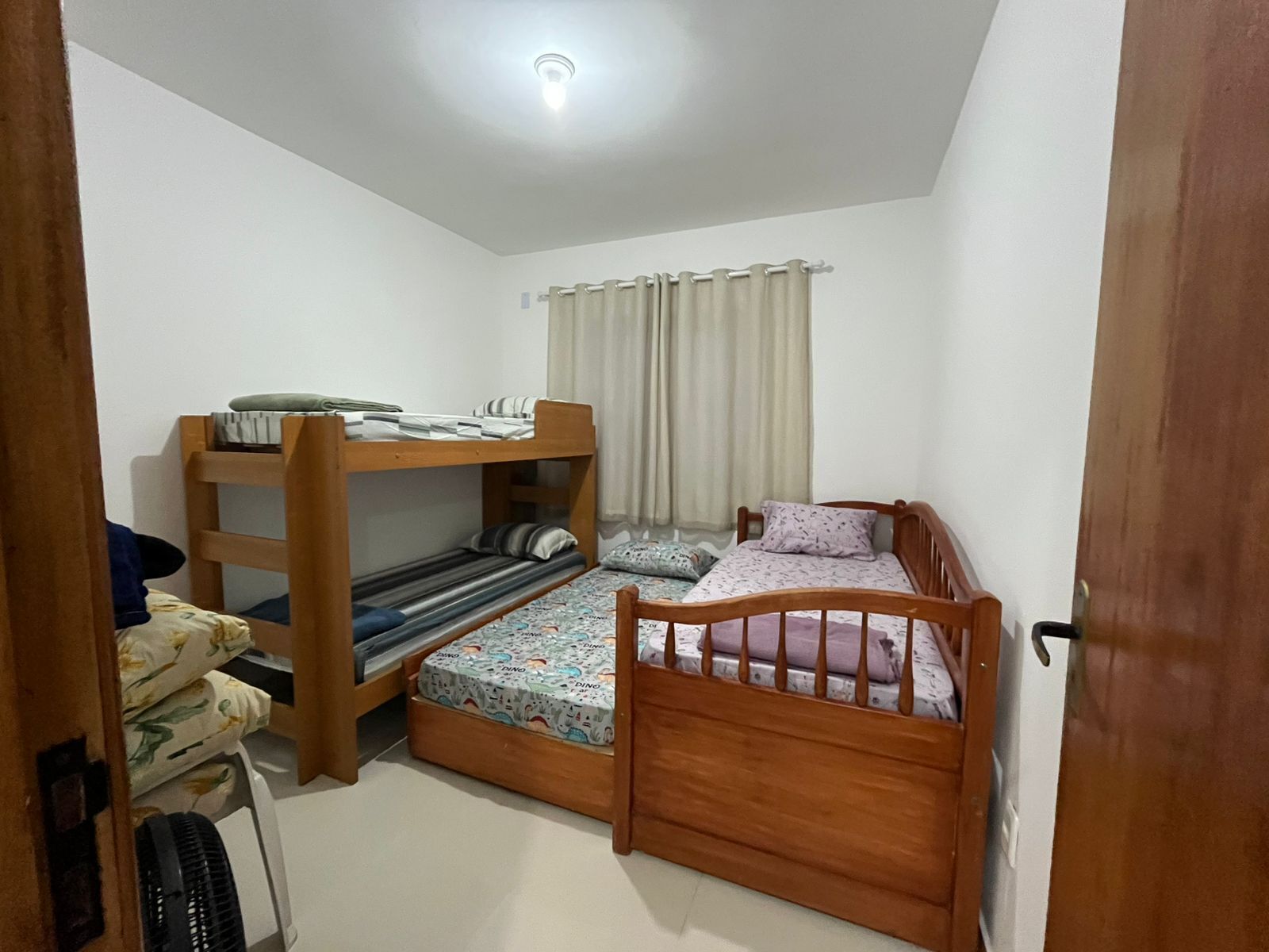 Habitación pequeña con literas, una cama individual, un ventilador y una ventana con cortinas.