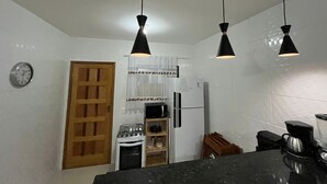 Une cuisine avec des murs recouverts de carreaux blancs, une porte en bois, une cuisinière, un réfrigérateur et trois lampes suspendues.