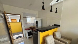 Une cuisine moderne avec un mur d’accent jaune, un plan de travail noir et un four encastré. On y trouve également un fauteuil beige et une petite table à manger avec des chaises.