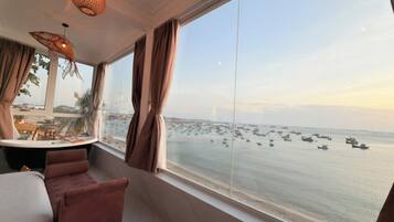 Una habitación con un ventanal grande con vista a un cuerpo de agua donde se ven barcos, una mesa redonda y un sofá.
