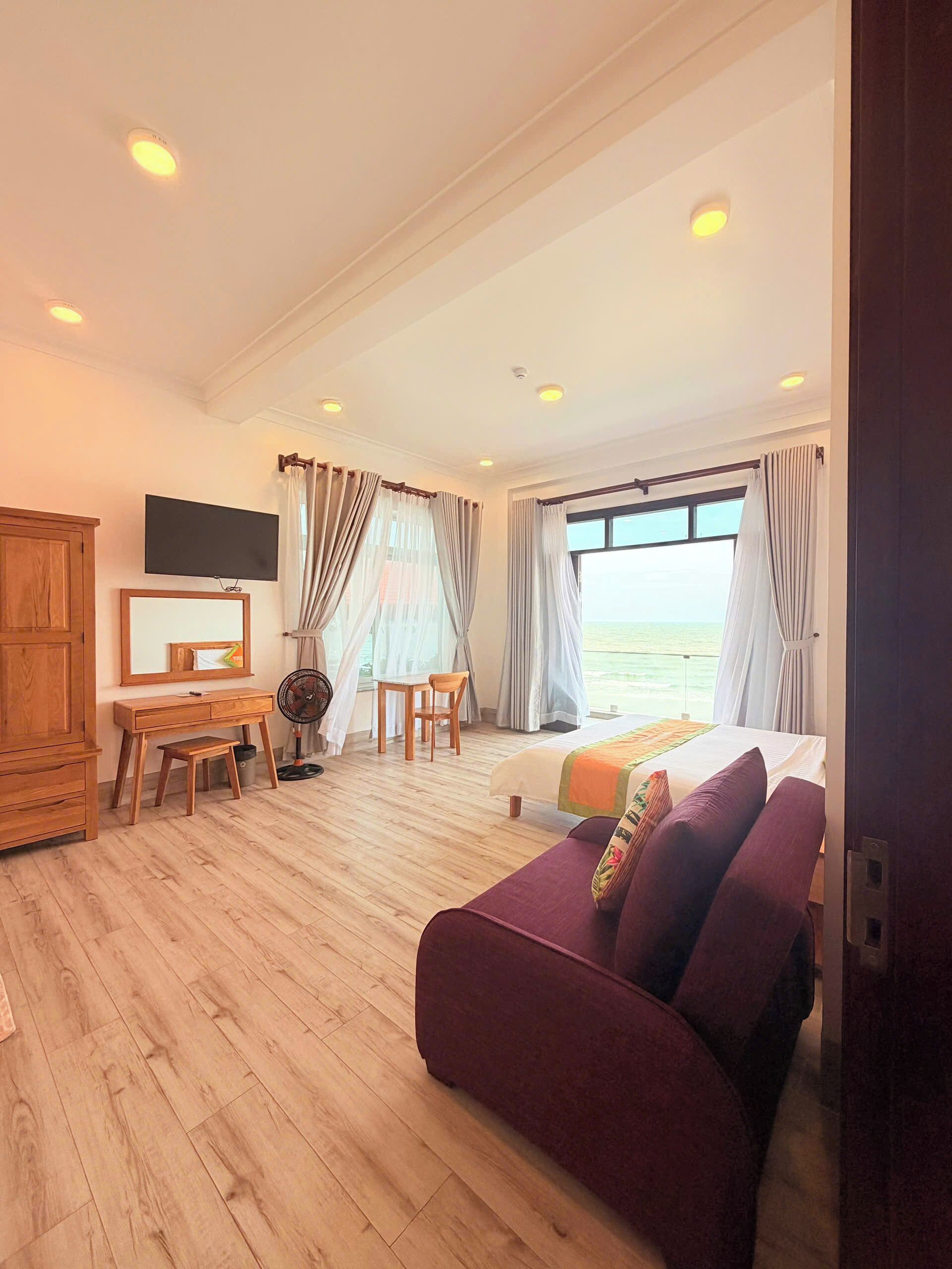 Une chambre d’hôtel avec un lit, un canapé, un bureau, une télévision et une vue sur la mer.