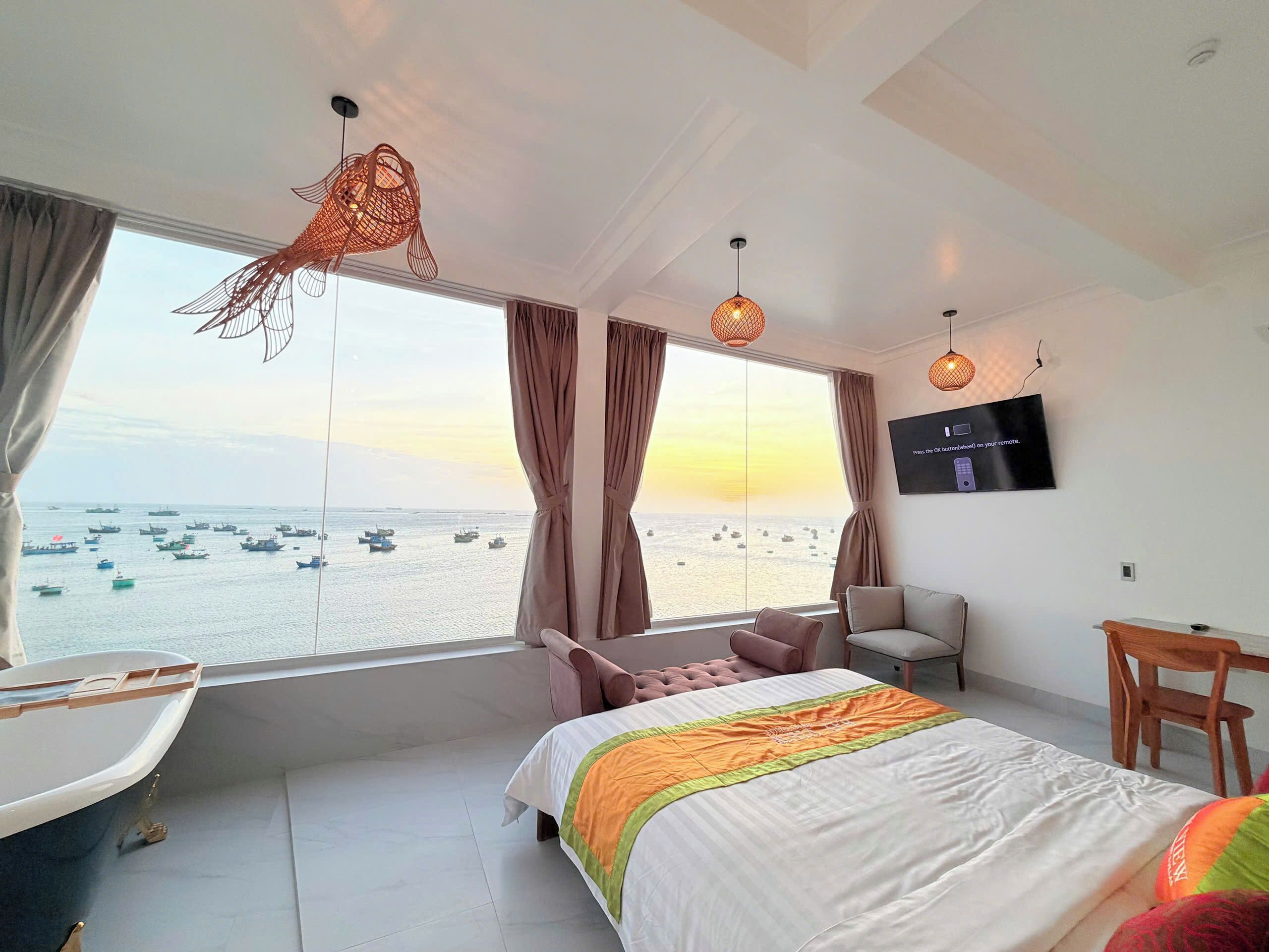 A hotel room with a large window, a bed, a TV, and a desk.