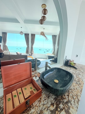 A modern bathroom with a large black sink, a wooden box with items, and a view of the sea through large windows. - BayView Resort & Villas (Mui Ne)