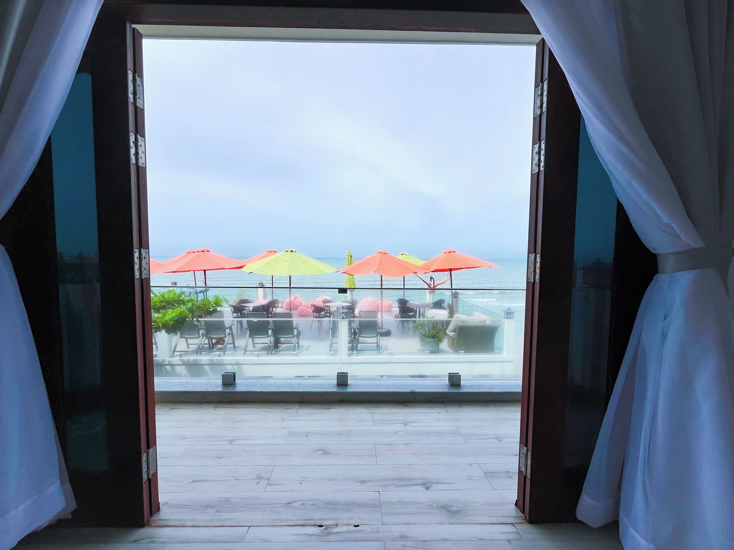 An open door leading to a terrace with outdoor seating and umbrellas, overlooking a body of water.