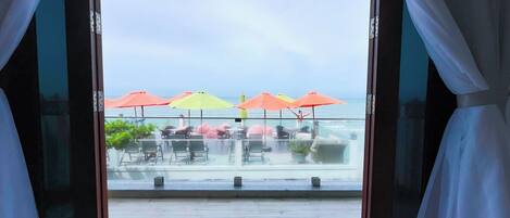 An open door leading to a terrace with outdoor seating and umbrellas, overlooking a body of water.