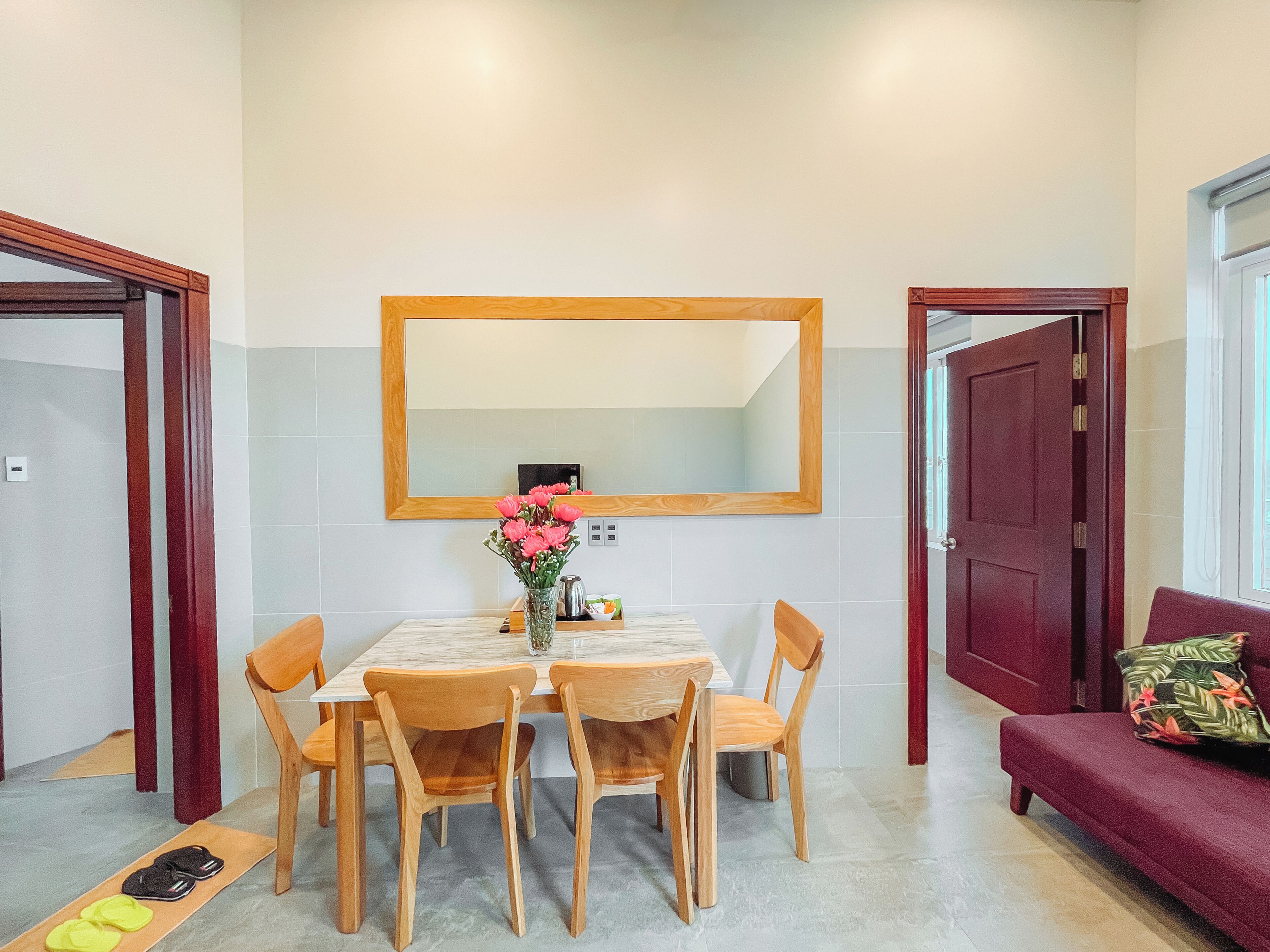 A dining area with a wooden table, chairs, a vase of flowers, and a red door.