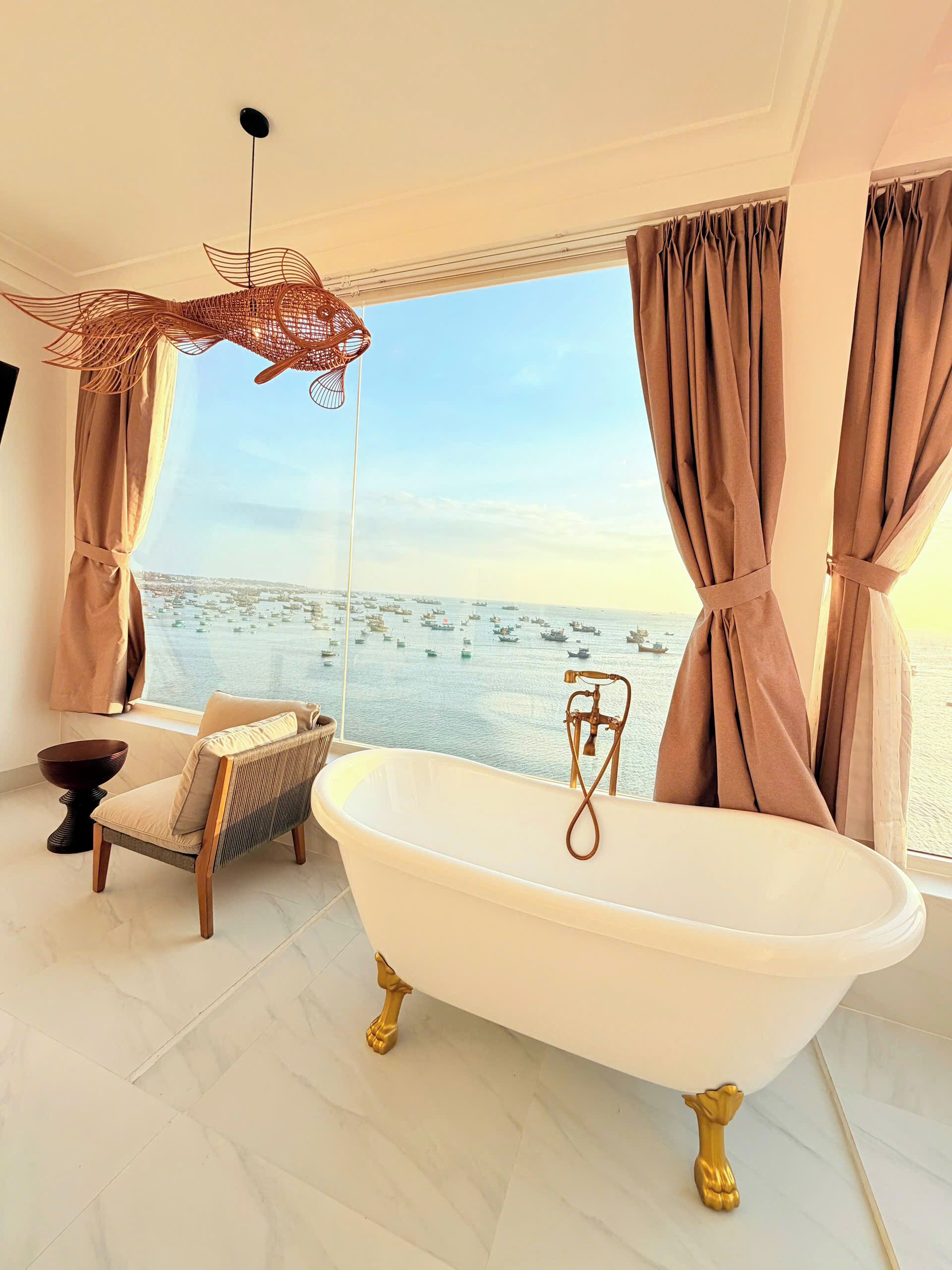 Une salle de bain moderne avec une baignoire sur pieds, une chaise en bois, un bol et une vue sur la mer.