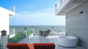 Un balcón con vista al mar, un jacuzzi y dos sillones de descanso.