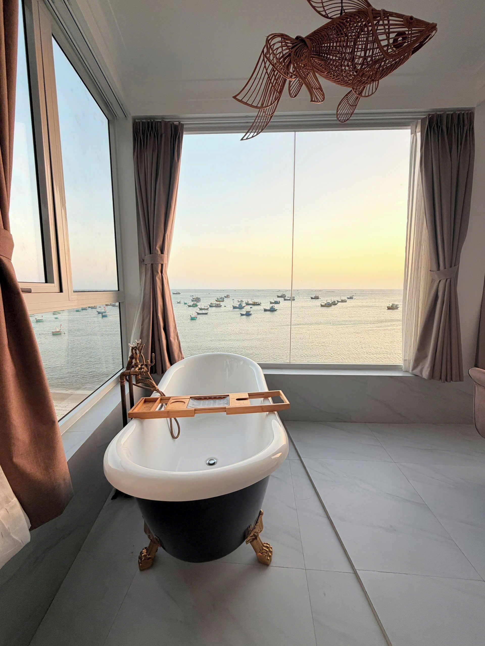 A bathroom with a bathtub, a wooden tray, and a view of the sea.