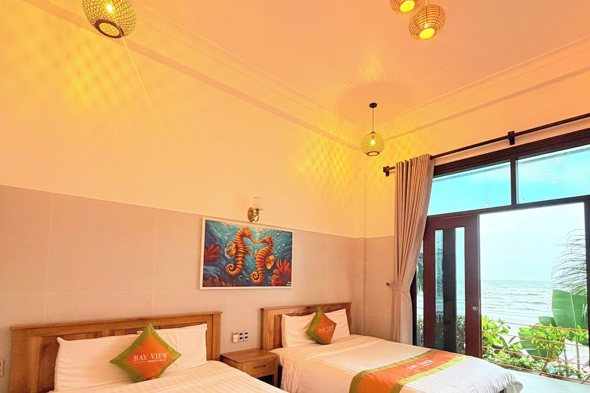 A hotel room with two beds, a painting, and a view of the sea.