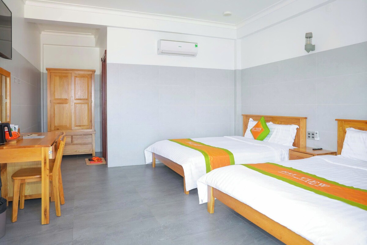 A hotel room with two beds, a wooden desk, a chair, and a wardrobe.