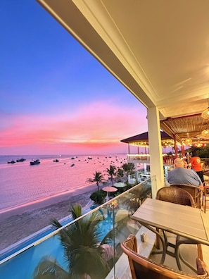 A balcony with a view of the beach and boats, a pool, and outdoor seating. - BayView Resort & Villas (Mui Ne)