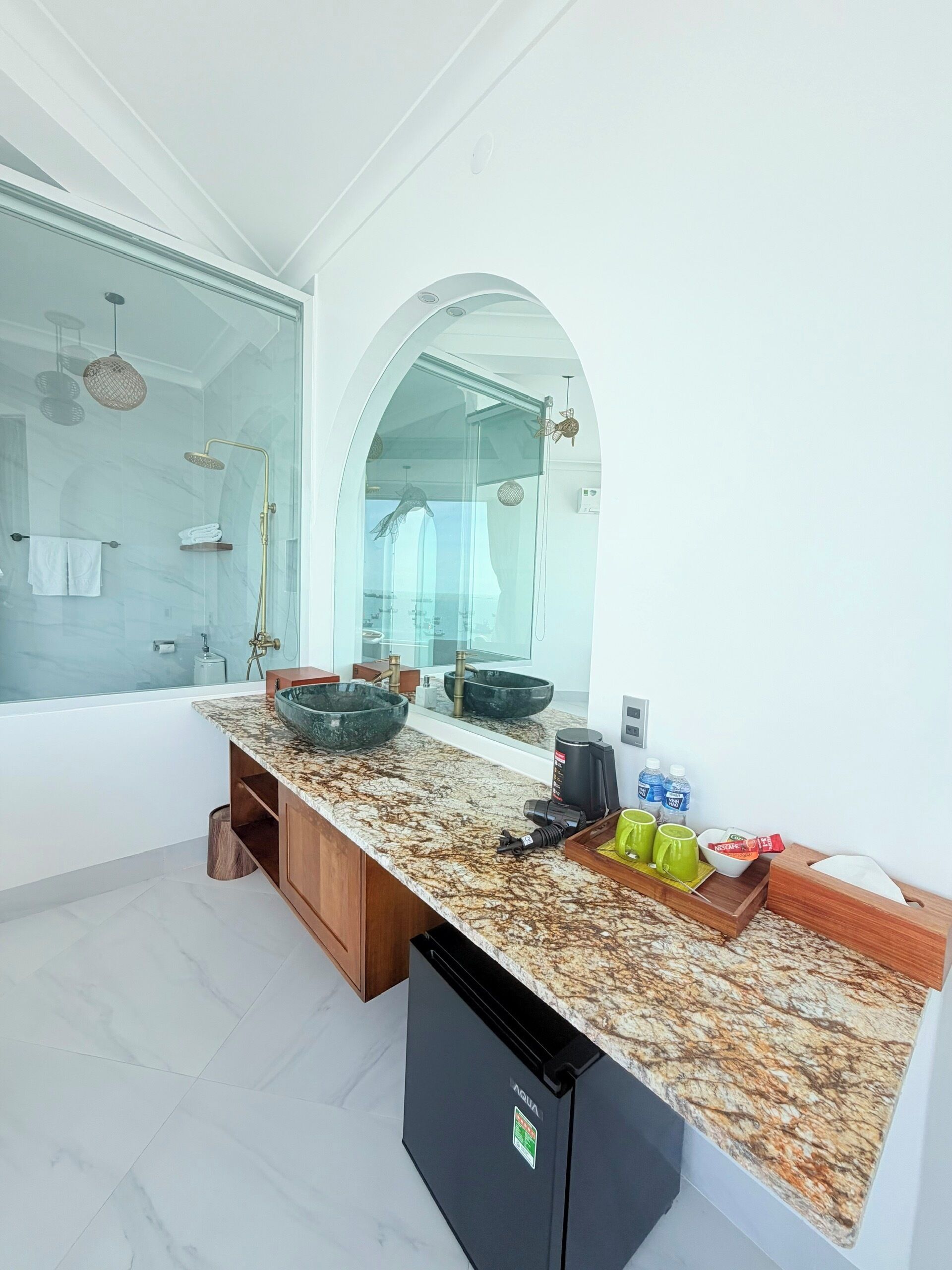 A modern bathroom with a glass shower enclosure, a marble countertop, and a black dishwasher.