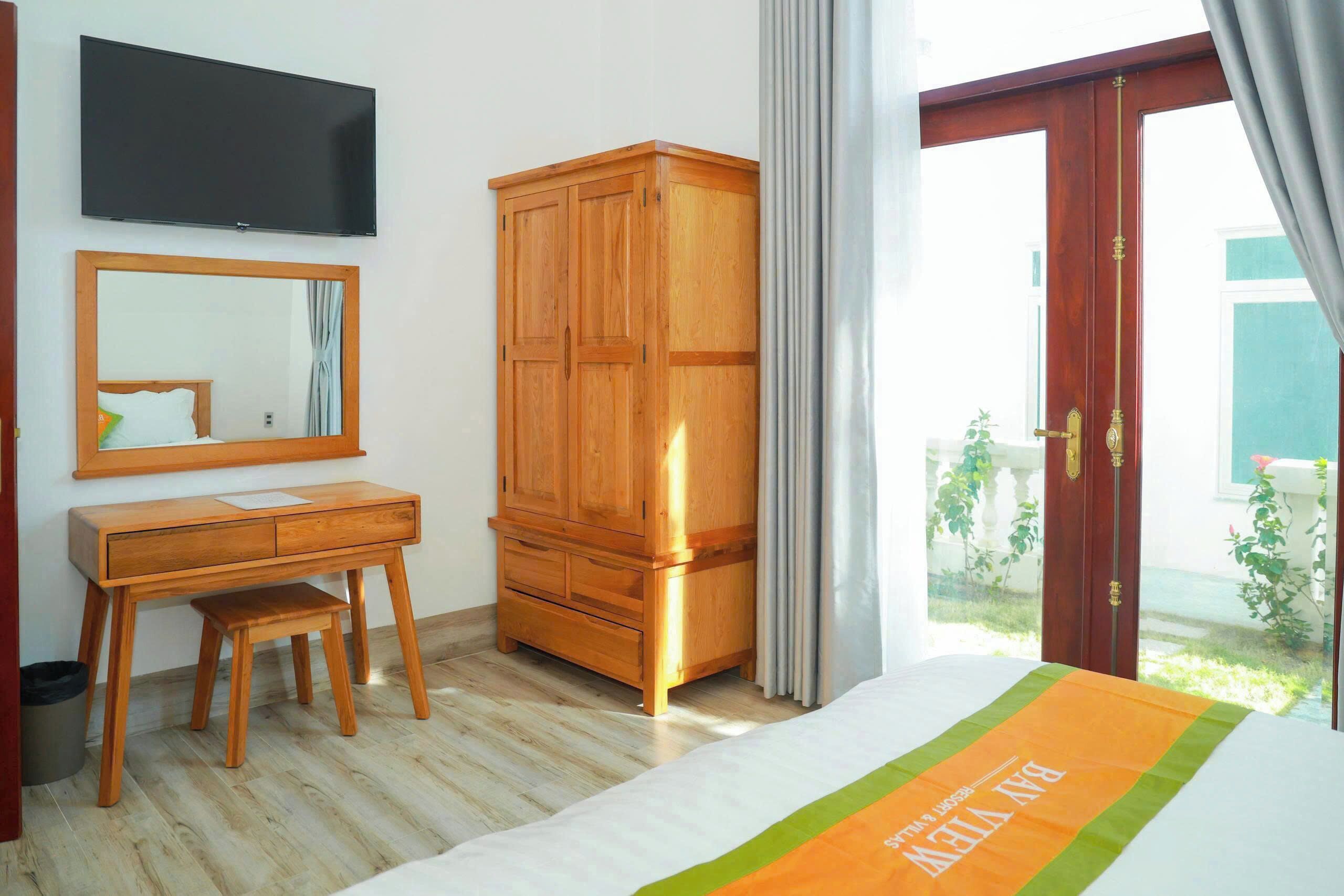Una camera da letto con un letto, una scrivania in legno, un armadio, una televisione e una finestra con tende.