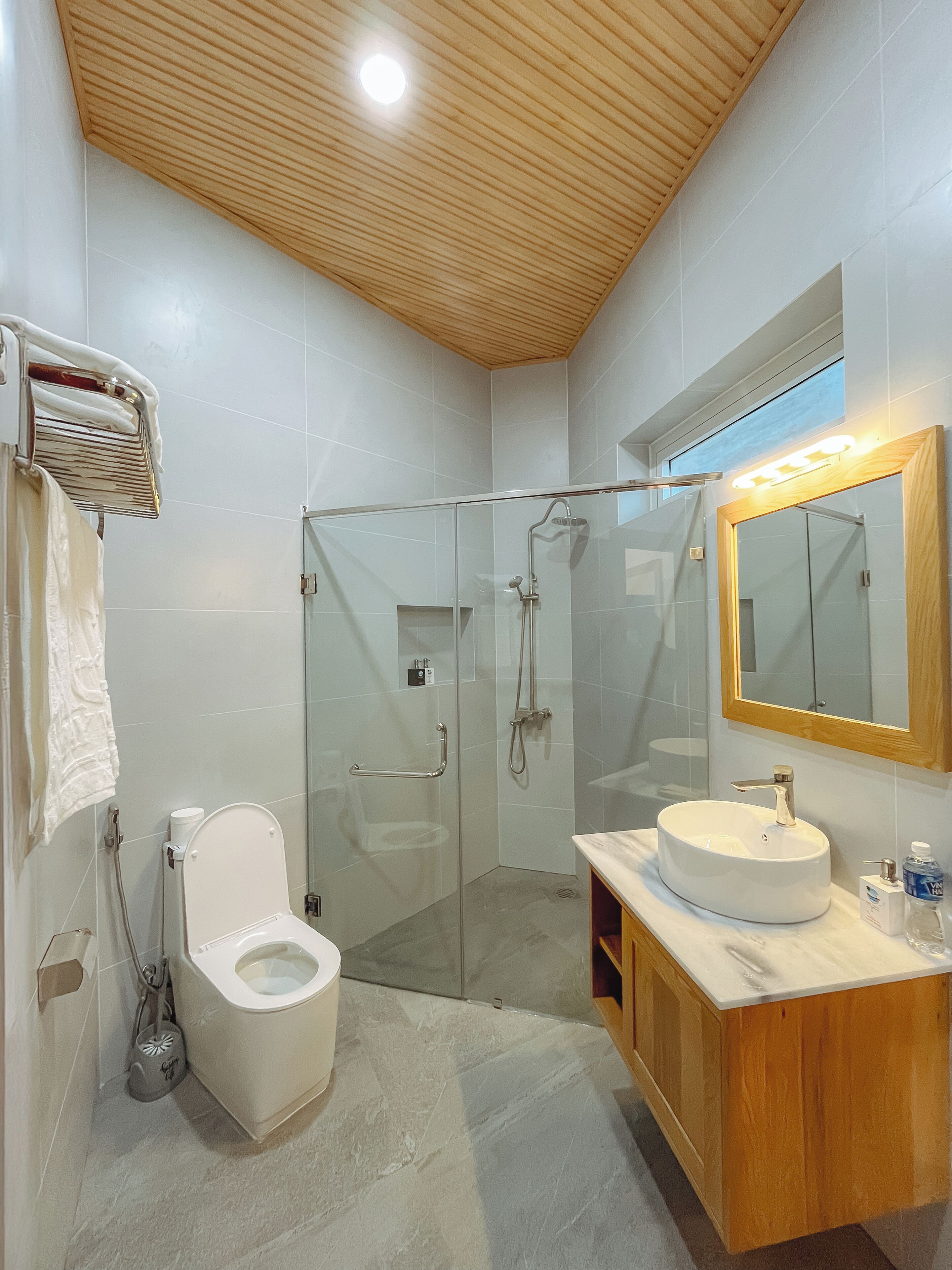 Un baño moderno con ducha envuelta en vidrio, inodoro blanco y tocador de madera con lavamanos redondo.